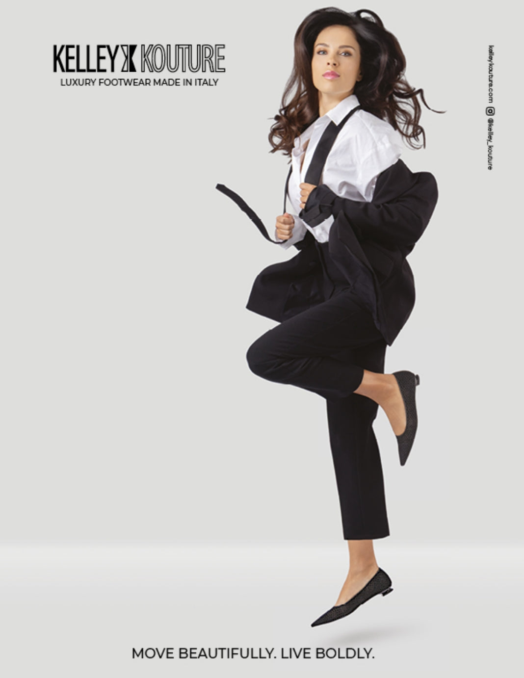 A model in a black blazer and black cropped trousers with a pair of Kelley Kouture Leona black flocked mesh pointed demi-wedge flat pump is posed dynamically against a light gray studio background. The brand name KELLEY KOUTURE is printed at the top left, and the slogan 'MOVE BEAUTIFULLY. LIVE BOLDY.'